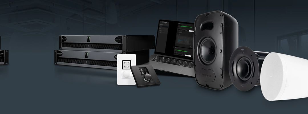 Professional audio gear: rack-mount amplifiers, large studio monitor speakers, a subwoofer, control panels, and a laptop displaying audio software on a dark backdrop.