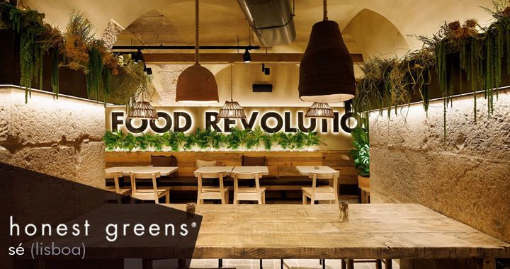 Restaurant dining area with wooden tables and benches, a back wall greenery, and a large 'FOOD REVOLUTION' sign.