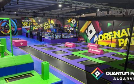 Indoor trampoline park with purple and green trampolines, foam blocks, and neon wall art; Quantum Park Algarve branding visible.