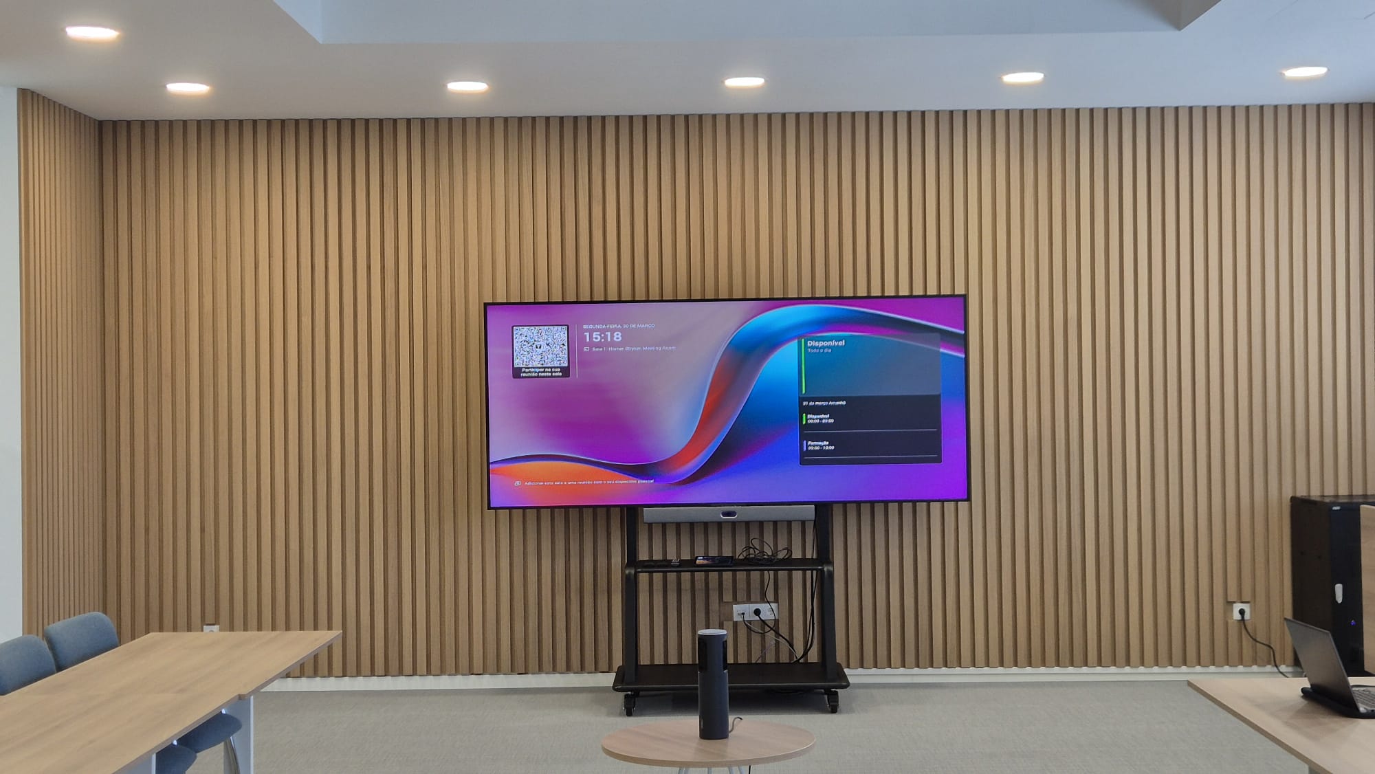 Conference room with a vertical wooden slat wall and a large mounted TV displaying a colorful desktop interface.