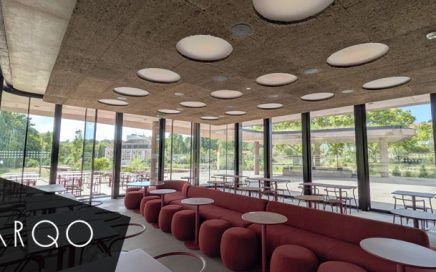 Modern glass-walled lounge with red ottoman seating and small white tables, circular ceiling lights overhead. ARQO branding visible in the corner.