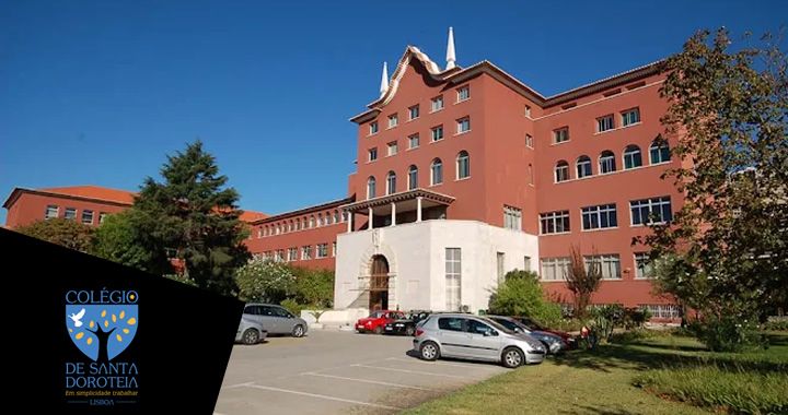 Exterior view of a red-brick school building with a white entrance stair and parked cars in a lot under a clear blue sky; blue school logo in bottom-left corner.