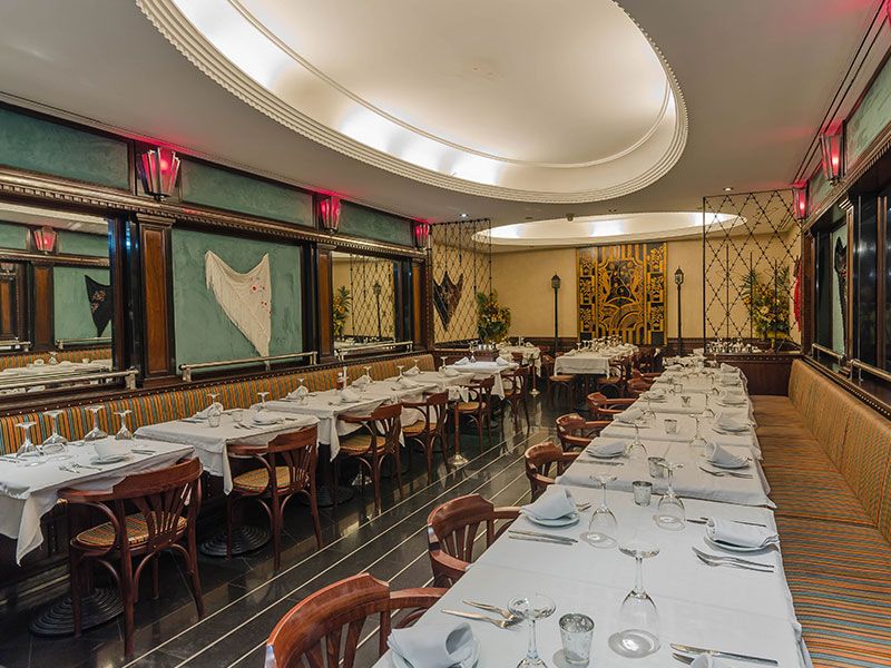 Elegant dining room set for a banquet with long white-clothed tables, glassware, and wooden chairs under warm ambient lighting.